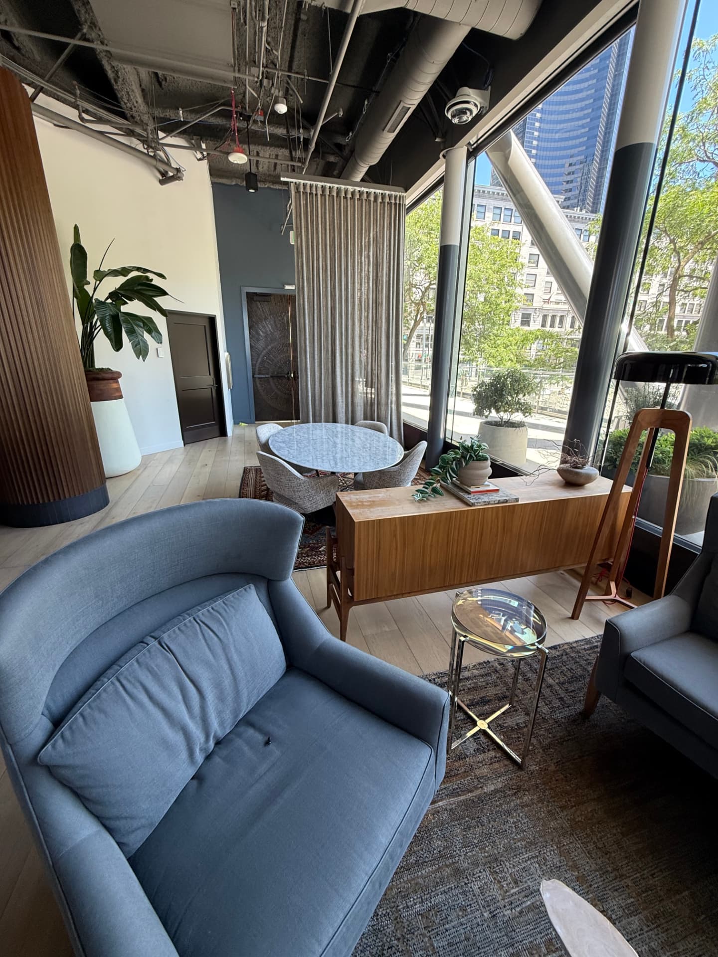 Cozy corner with a soft blue armchair, wood credenza, and marble table by the windows.