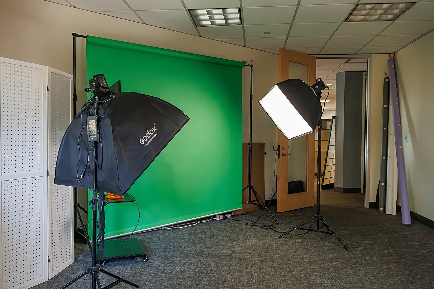 Studio corner with a green screen backdrop and two Godox softbox lights on stands.