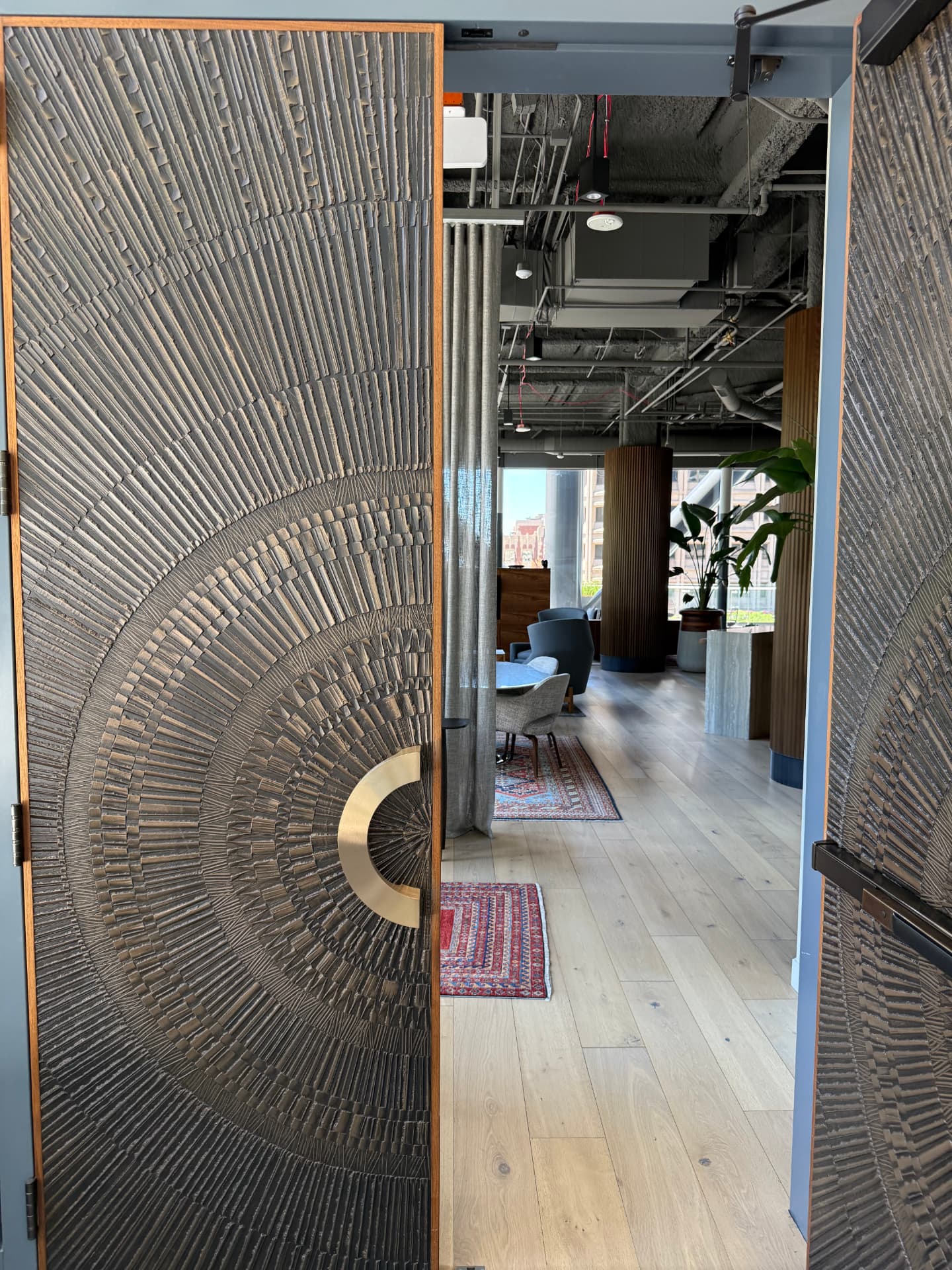 Sculpted bronze sunburst doors opening onto the tenant lounge with rugs and lounge chairs beyond.