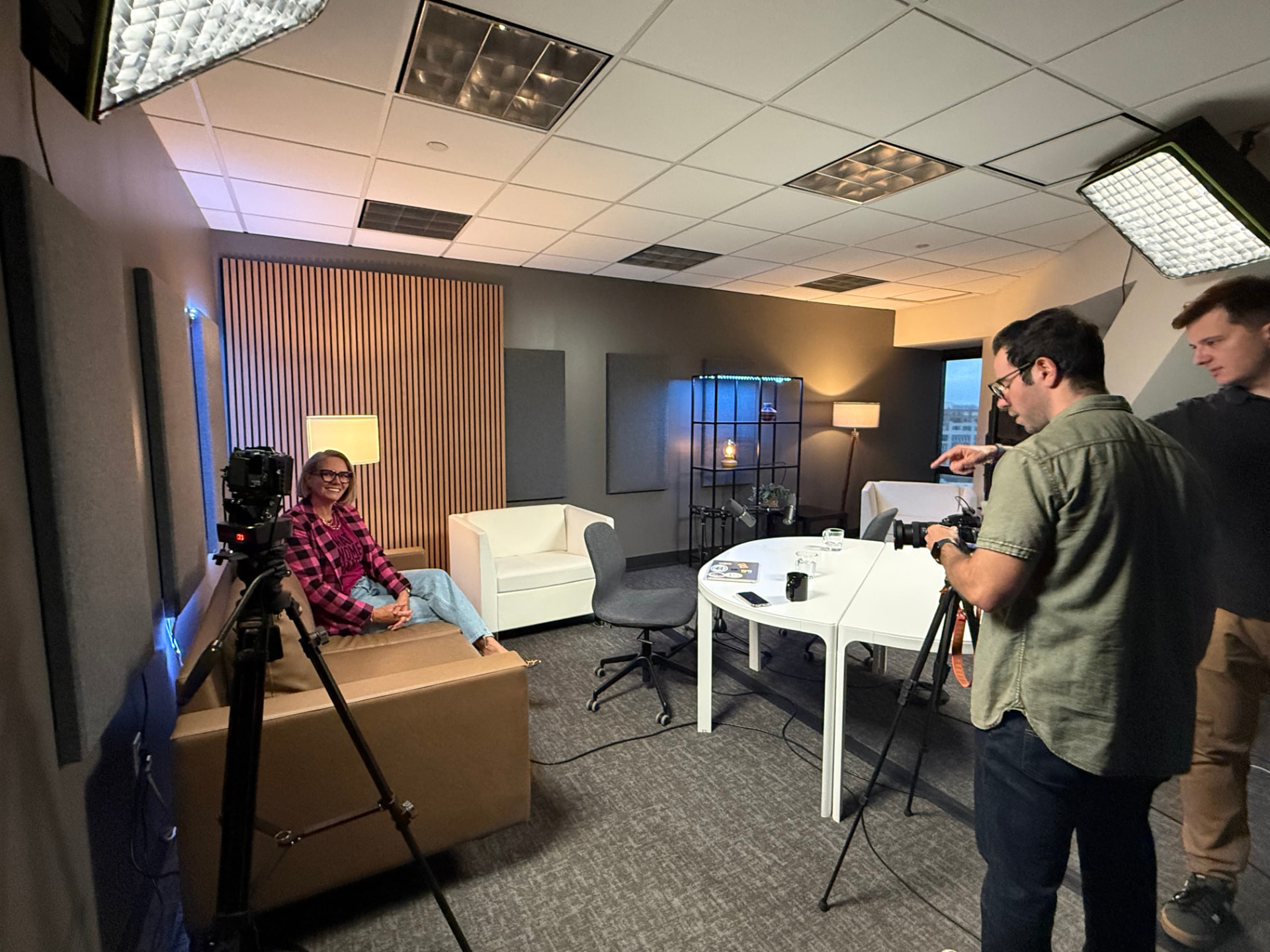 Video shoot in progress with a guest seated on a leather chair, two operators behind cameras, and softbox lights overhead.