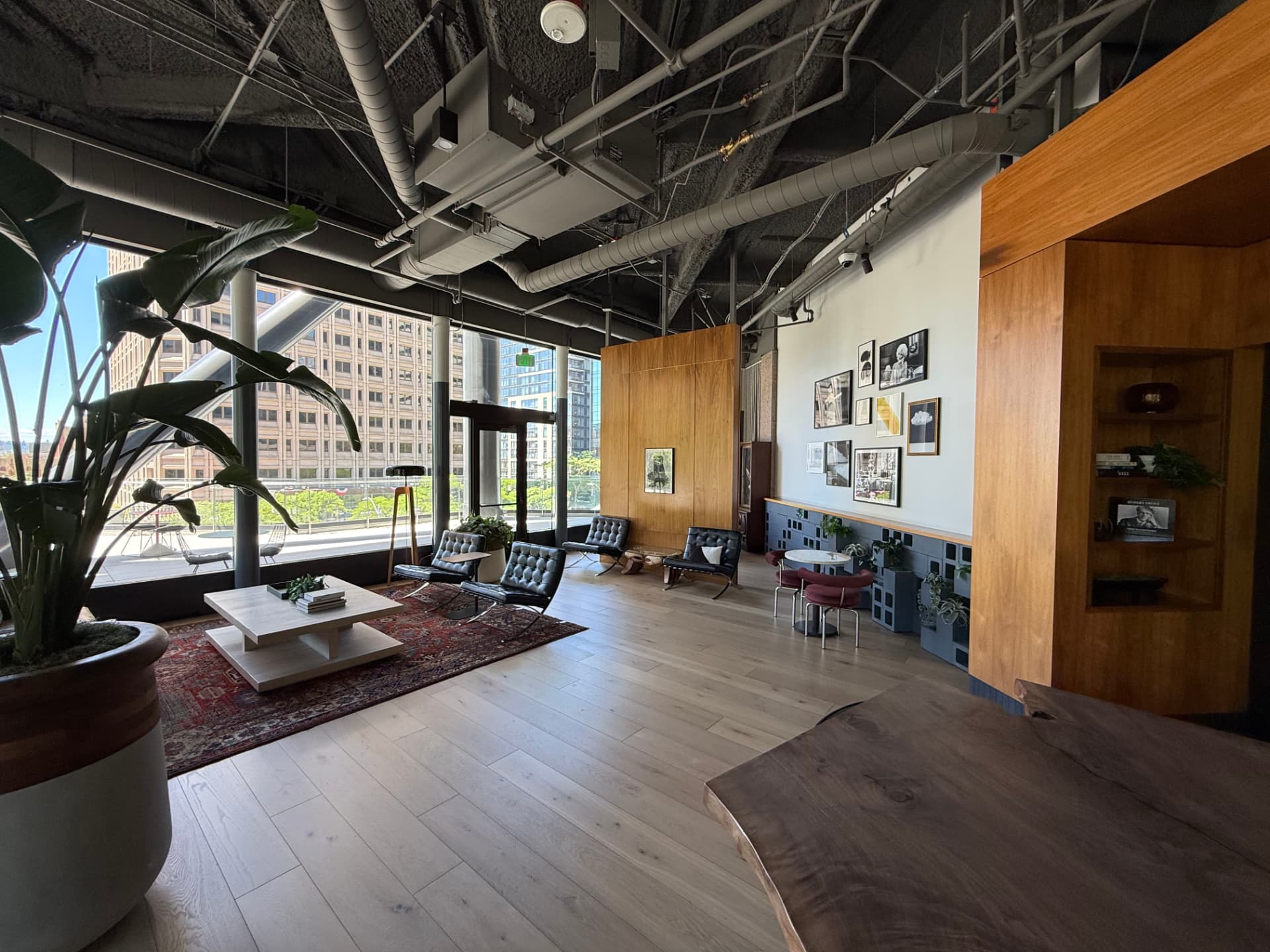 Lounge with black leather chairs, a Persian rug, gallery-wall of framed photography, and city views.
