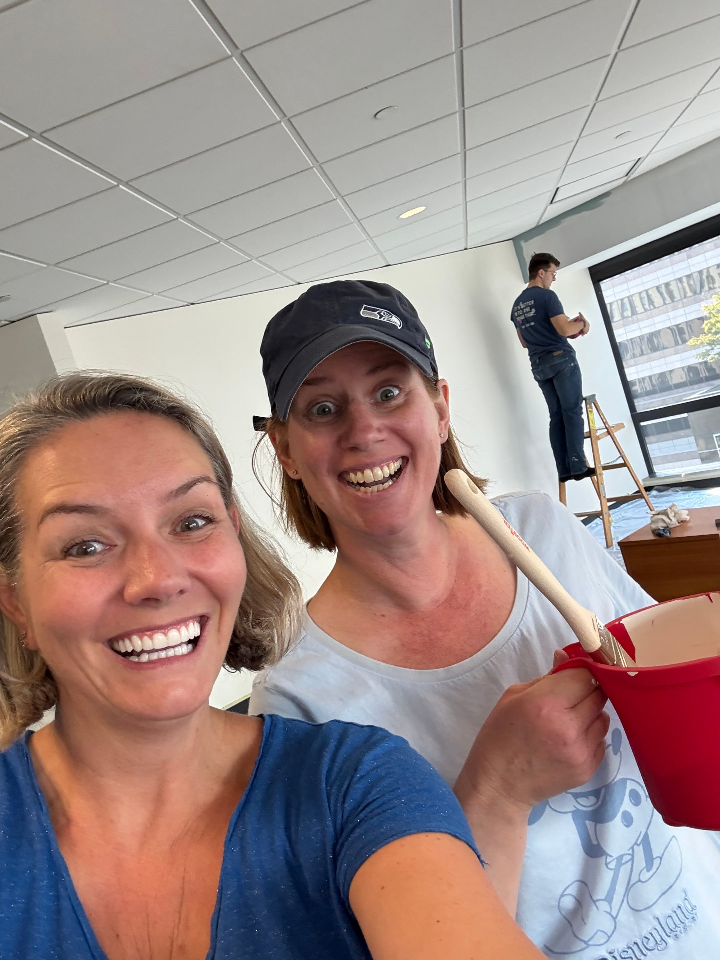 Sally and a friend mid-paint, laughing with a roller in hand