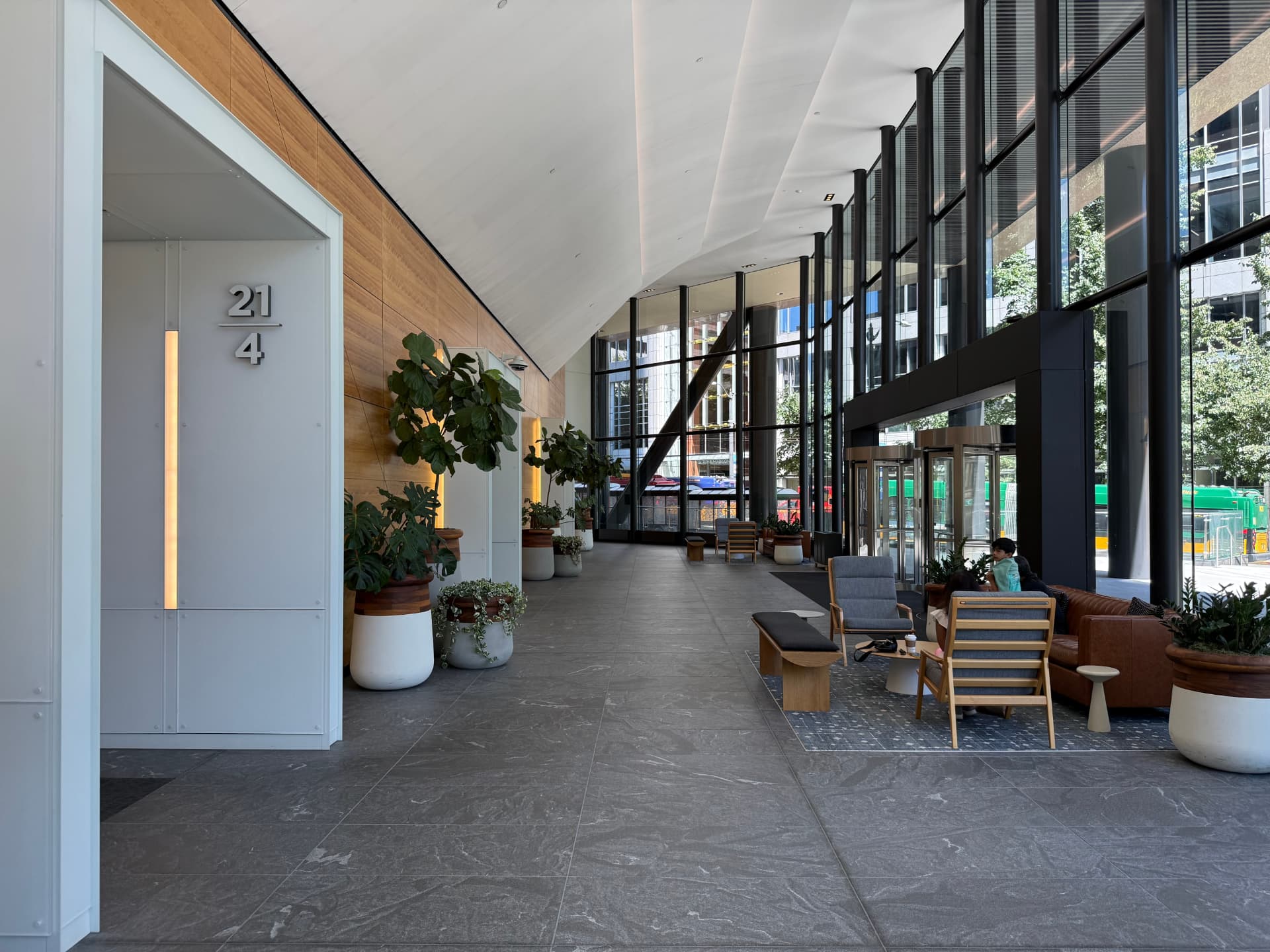 Ground-floor lobby of 999 3rd Avenue with high ceilings, wood paneling, planters, and lounge seating by the windows.