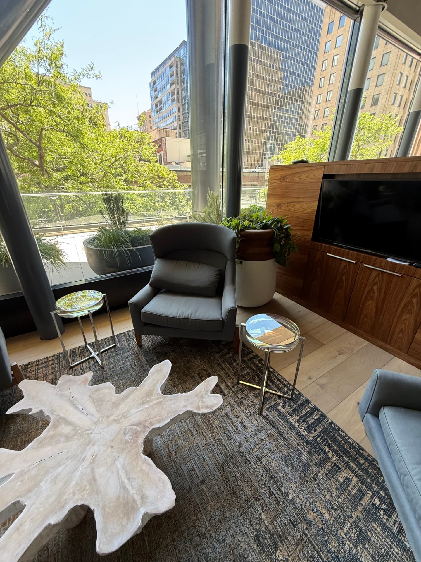 Lounge nook with a grey armchair, side tables, a wall-mounted TV, and terrace views.