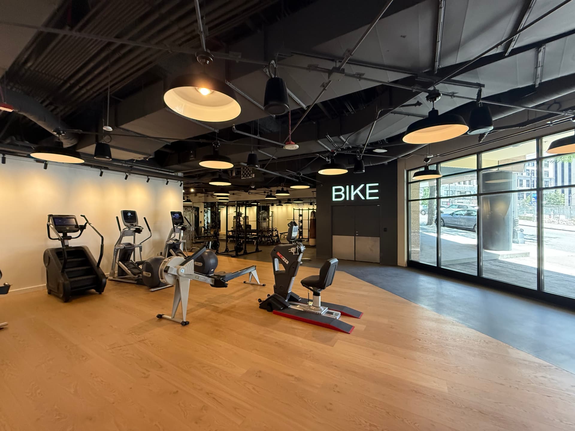 Modern gym cardio floor with rowing machines, ellipticals, and a neon BIKE sign.