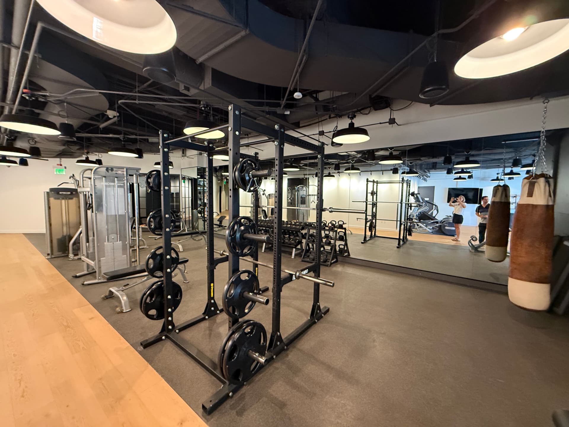 Weightlifting area with a power rack, dumbbells, a heavy bag, and large mirrors.