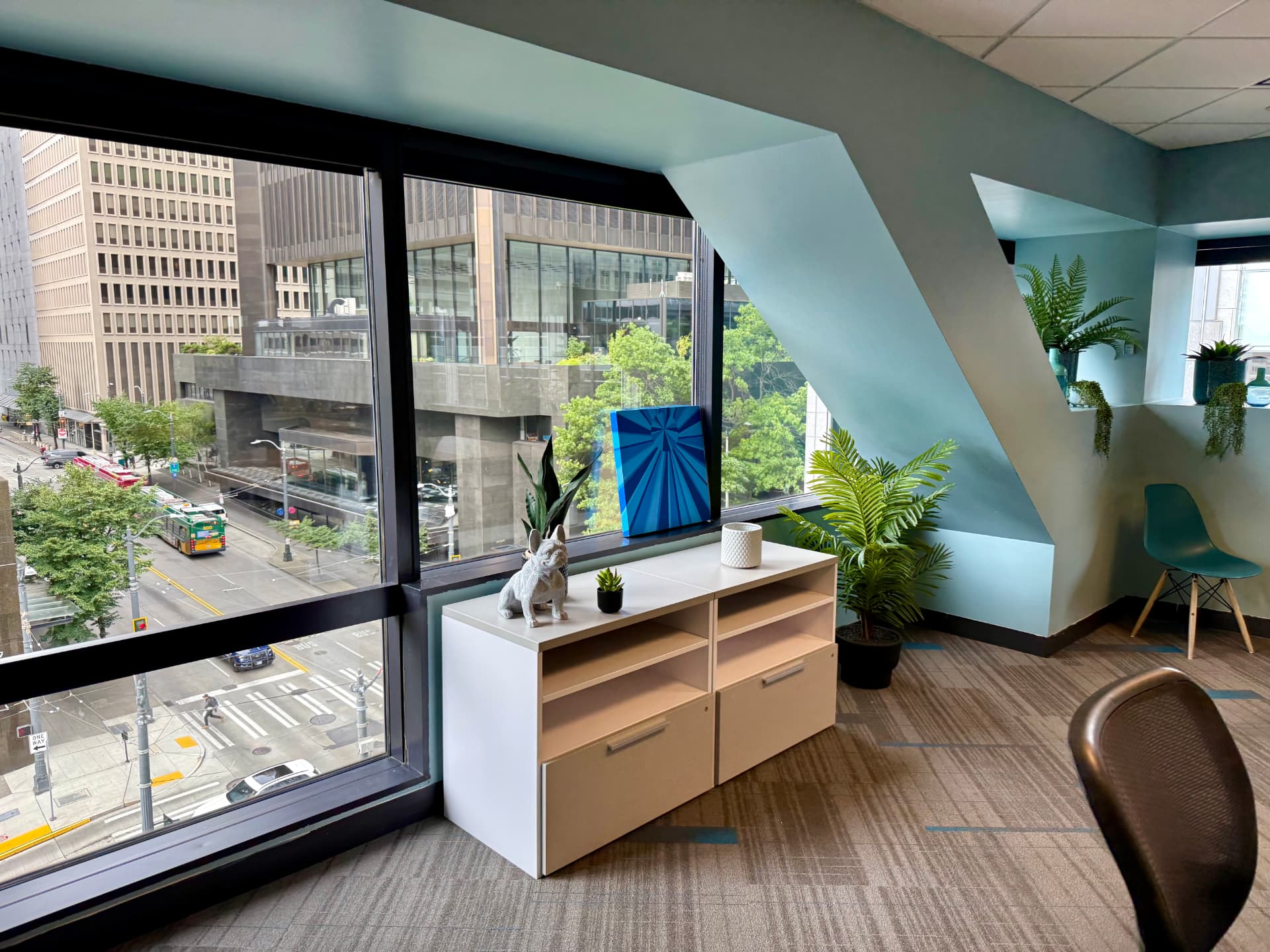 Lounge detail showing a white shelf with decor and a blue painting in front of a window overlooking a city street.