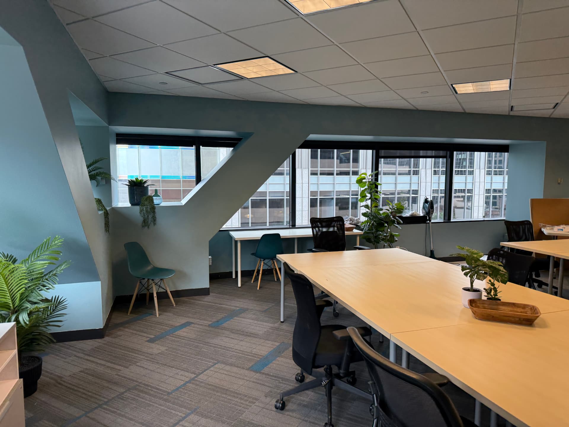 Corner coworking table by a large window with a view of tall city buildings.