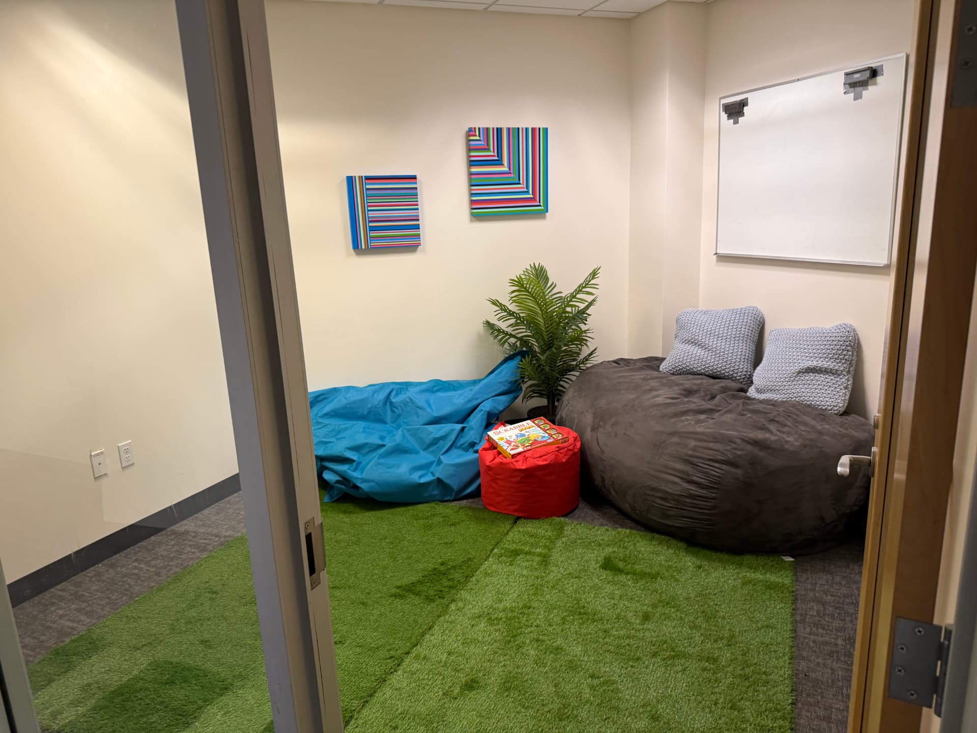 Kids hangout and lactation room with bean bags, a green rug, a whiteboard, and potted plants.